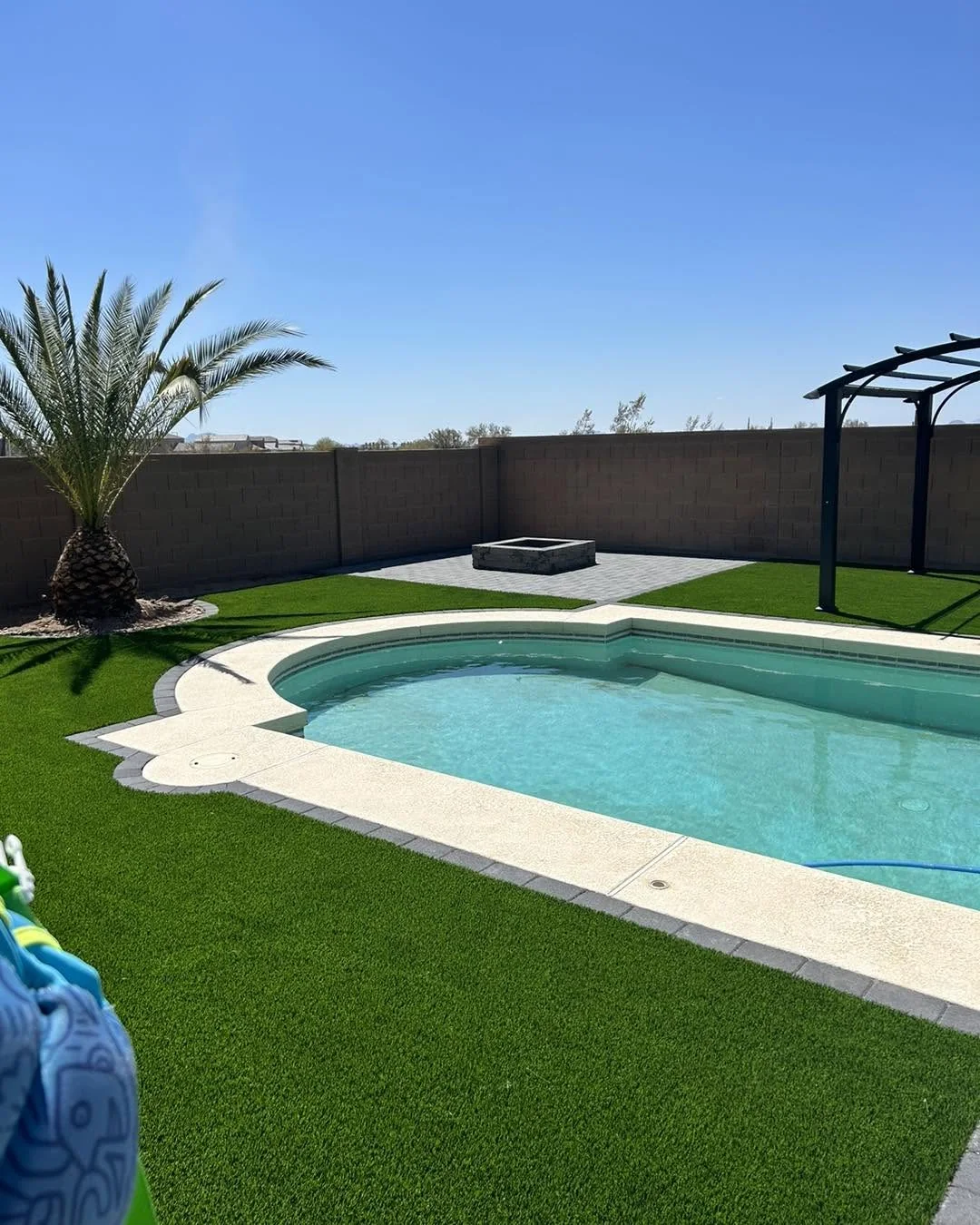 Buckeye-area backyard with artificial turf, pool, paver border, fire pit, and pergola